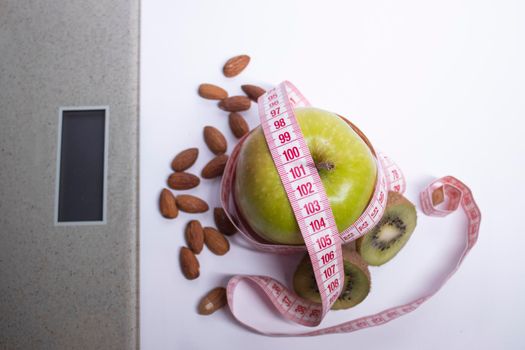 Red measuring tape, apple, kiwi and almonds near beige bathroom scales. Diet and Healthy life, loss weight, sport concept. Top view. Copy space. Isolated. White background