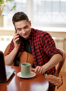 Man on kitchen playing the guitar with laptop at home