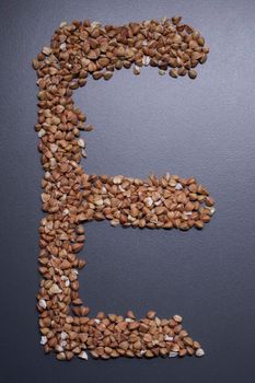 Letter 'E' written with buckwheat On gray background, top view, copy space. Food supplies crisis, food donation on quarantine isolation period