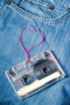 vintage audio cassette on blue jeans with red tape pulled out as heart shape