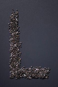 Letter 'L' written with chia seeds on gray background, top view, copy space.