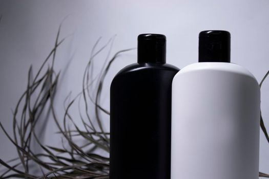 Composition of two white and black shampoo bottles with no label near dried leaves. body care and beauty concept. Copy space. . High quality photo