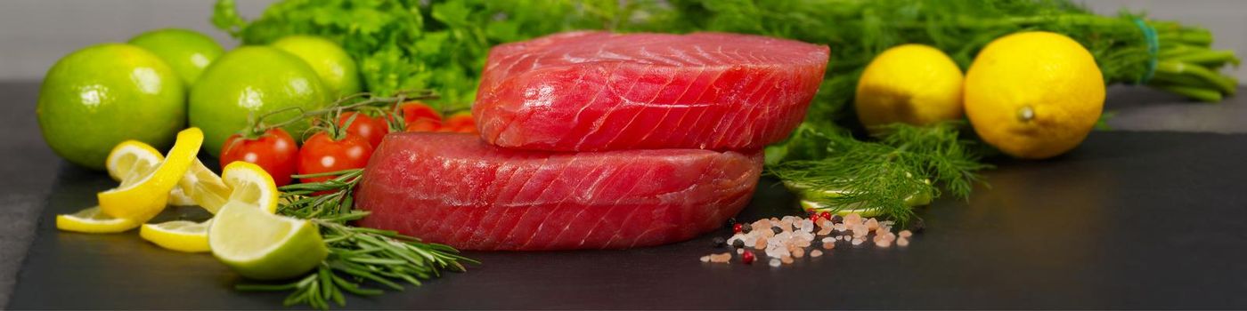 Tuna raw Steak, tuna sashimi, tuna fish sliced with vegetables. Healthy eating with seafood, we cook at home. Cooking receipt concept, fish menu, fish meat layout on black stone, banner