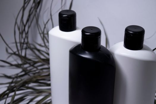 Composition of three white and black shampoo bottles with no label near dried leaves. body care and beauty concept. Copy space. . High quality photo