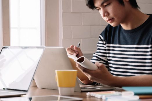 Close up of male student busy studying using laptop make notes in notebook while write watching webinar or online training course on computer, education concept.