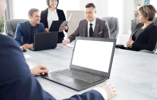 Laptop against the background of a group of young business people in the office discussing a work idea together. 