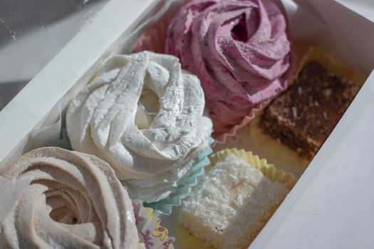 Sweet homemade dessert zephyr pink, beige, white - big marshmallows and 'bird milk' candies in a white gift box on a white table. handmade Big zephyr sprinkled with powdered sugar. Food photography