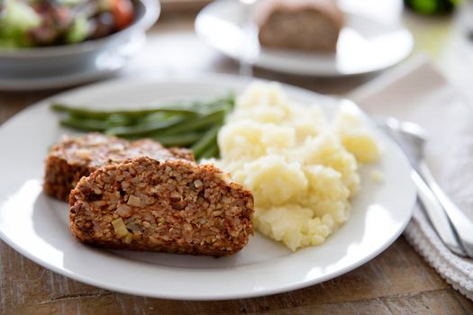 Slices of vegan lentil loaf with mashed potatoes and green beans.