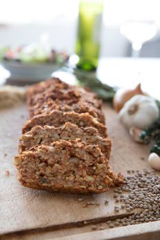 Slices of lentil loaf on cutting board with ingredients, vertical orientation.