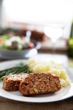 Slices of vegan lentil loaf with mashed potatoes and green beans.