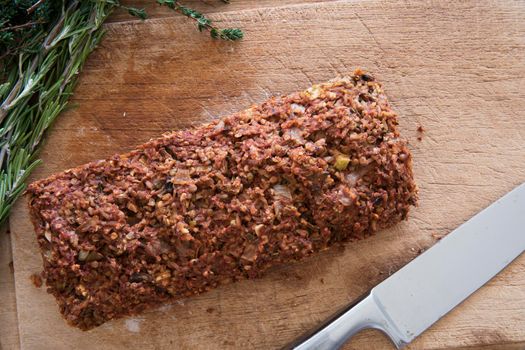 Lentil loaf on cutting board with herbs and knife, view from above.