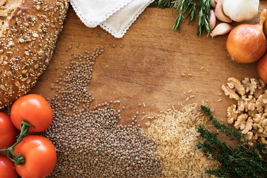 Healthy food frame with fresh vegetables, herbs and grains on rustic wooden background viewed from above.