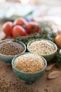 Healthy grains, brown rice, lentils and oats in bowls with veggies in the background.