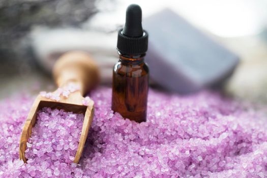 Purple bath salts with wooden scoop and bottle of essential oil