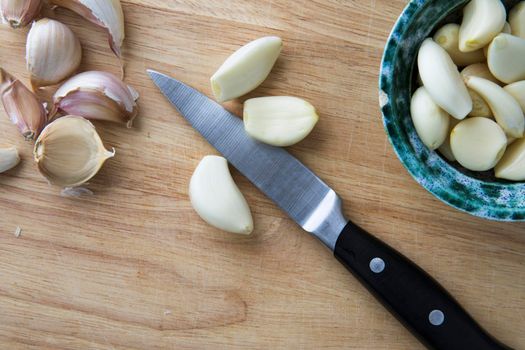 Peeled garlic cloves on cutting board with knife and bowl fro from directly above.
