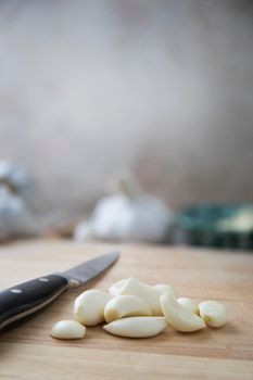 Peeled garlic cloves on wooden cutting board beside knife vertical layout.
