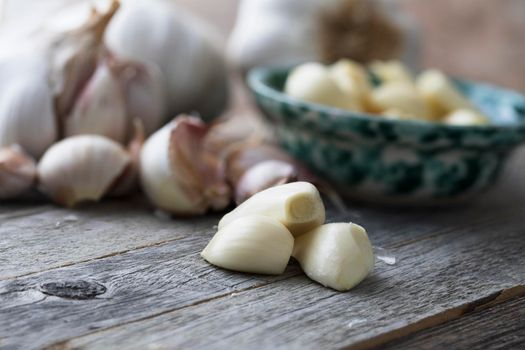 Close up of peeled garlic cloves with garlic head and unpeeled cloves in background.