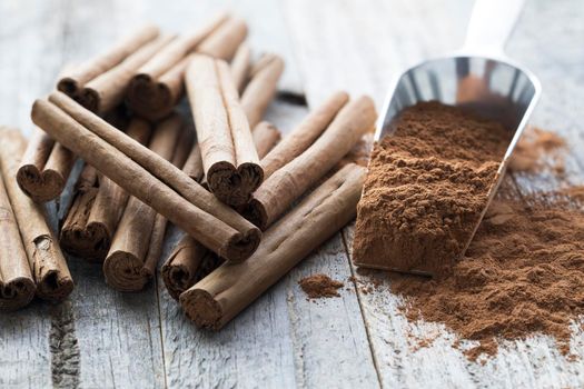 Metal scoop filled with ground cinnamon sitting beside whole cinnamon sticks.