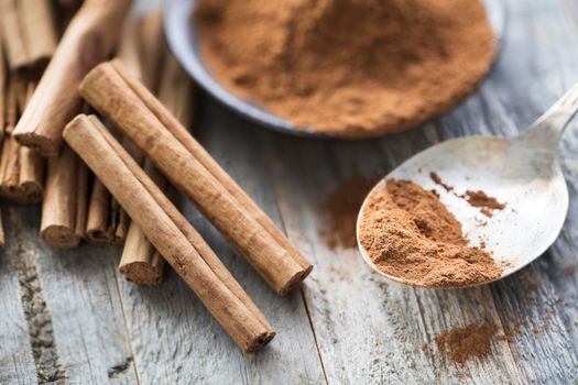 Close up of ground cinnamon on spoon with whole cinnamon sticks.