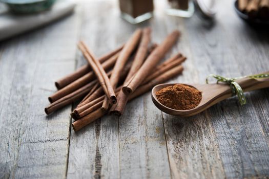 Wooden spoon filled with ground cinnamon on rustic wooden surface with cinnamon sticks.