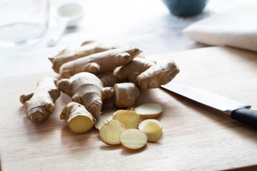 Ginger root and ginger slices with knife on cutting board.