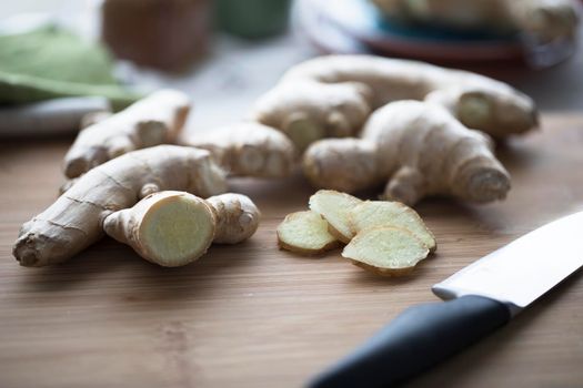 Ginger root and ginger slices with knife on cutting board.