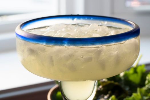 Close up of margarita on ice in glass with blue rim.