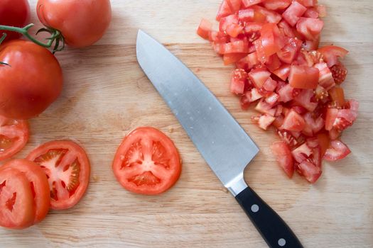 Tomatoes, whole, sliced and chopped, on cutting board with knife.