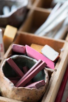 Pot of conte sticks and erasers in artist supply tray.