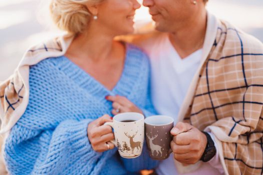 Smiling couple wrapped in a plaid and holding cups in their hands on a background of mountains. High quality photo