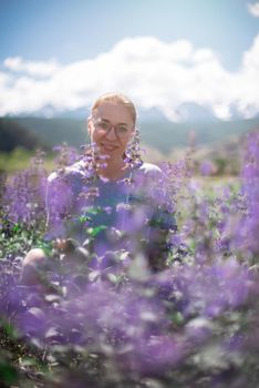 Happy young woman in beautiful wild pink and purple flowers field in summer Altai mountains