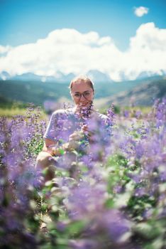 Happy young woman in beautiful wild pink and purple flowers field in summer Altai mountains