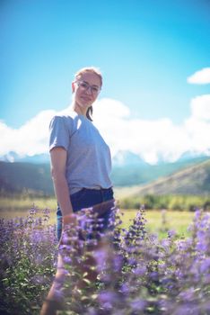 Happy young woman in beautiful wild pink and purple flowers field in summer Altai mountains