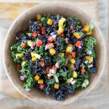 Healthy kale salad with fresh bell peppers and red onions in a wooden bowl viewed from above.