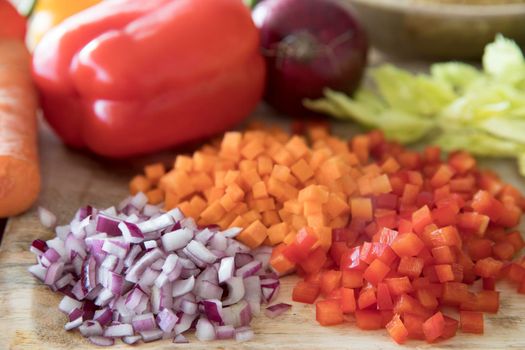 Red bell pepper, carrots and onions diced on a cutting board.