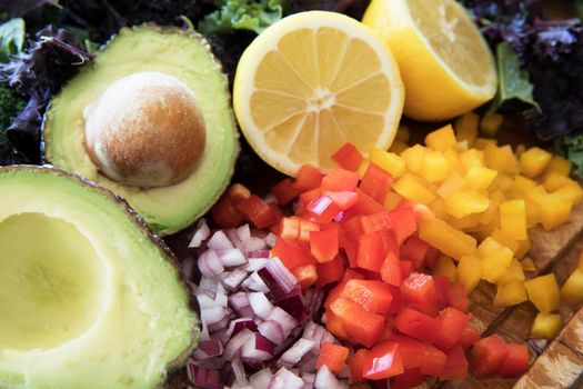 Ingredients for a healthy salad including bell peppers, onions, avocado, lemons, and kale.