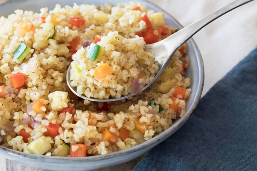 Spoonful of vegan bulgur pilaf with carrots, red peppers, onions and zucchini.