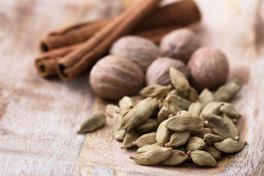 Cardamon seeds with nutmeg and cinnamon sticks on rustic wooden surface.