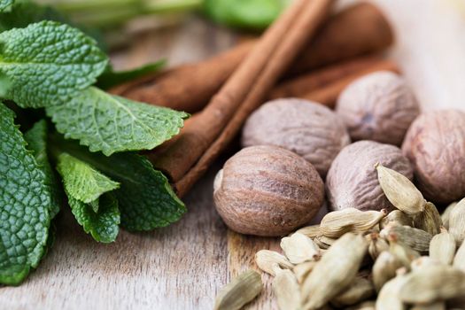 Cardamon, nutmeg, mint leaves and cinnamon sticks close-up on rustic wooden surface