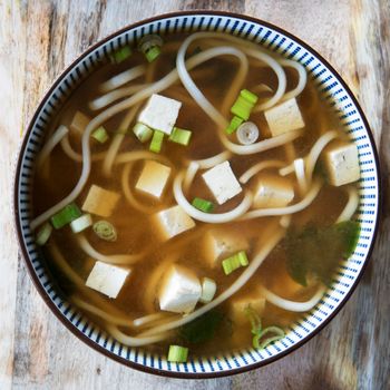 Red miso soup with tofu, green onions and udon noodles.  Square orientation, close-up flat lay.