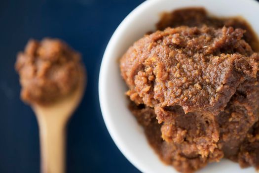 Red miso paste on white bowl viewed from above with spoon on table out of focus.