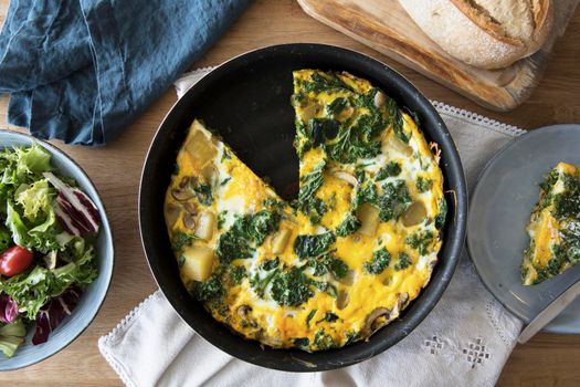 Delicious frittata with kale and potatoes in pan with slice removed viewed from above.