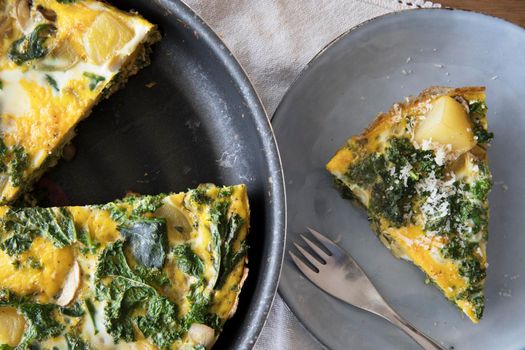 Delicious frittata with kale and potatoes in pan and slice on plate.
