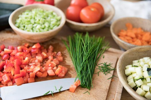 Chopped tomatoes and chives on cutting board with knife surrounded by other ingredients.