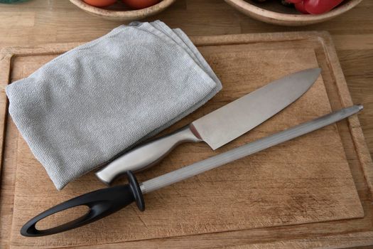 Chef's knife, honing steel and towel on cutting board, preparing for knife honing.