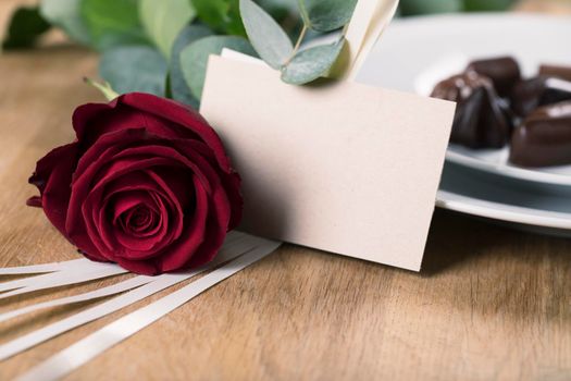 Close up of red rose and blank card with plate of chocolates in the background