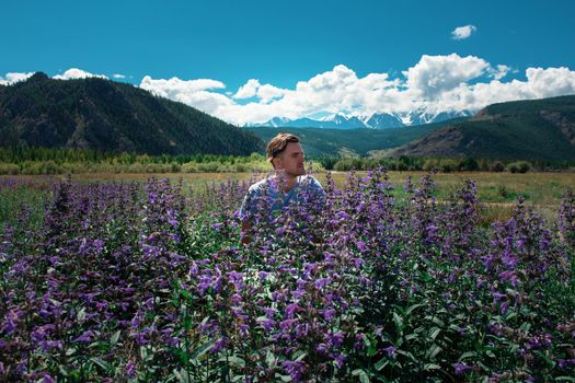 Man in beautiful wild pink and purple flowers field in summer Altai mountains