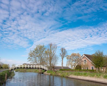 footbridge and old farm along river Lange Linschoten in the netherlands near Ouderwater under blue sky in spring