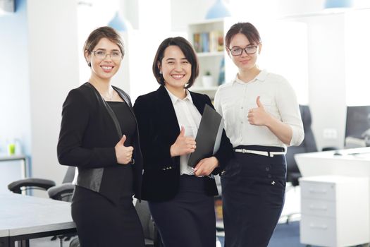Three young successful business women in the office smiling happily. 