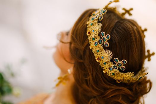 A woman with a beautiful hairstyle in a gold crown with stones, close-up. Bride wearing a crown on an orthodox wedding . High quality photo